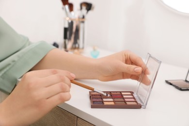 Photo of Woman with eyeshadow palette and brush at dressing table indoors, closeup