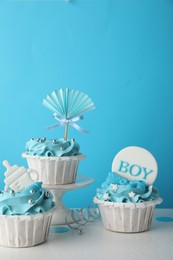 Photo of Baby shower cupcakes with toppers on white table against light blue background