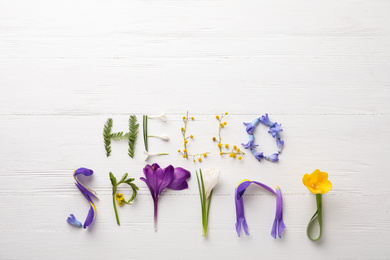 Photo of Words HELLO SPRING made of fresh flowers on white wooden table, flat lay