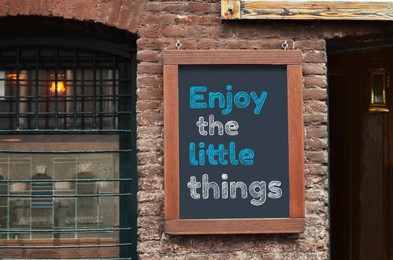Image of Inspirational vibes. Board with phrase Enjoy Little Things on building