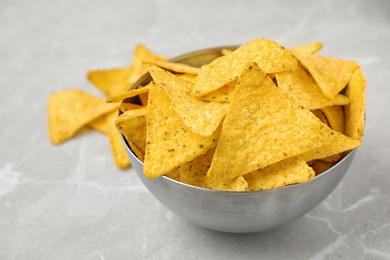 Photo of Metal bowl with tasty Mexican nachos chips on grey table