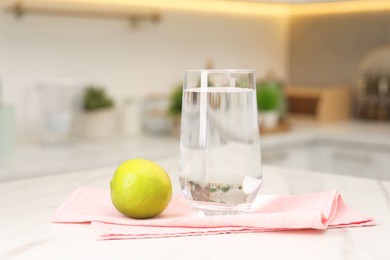 Photo of Filtered water in glass and lime on white marble table in kitchen, closeup