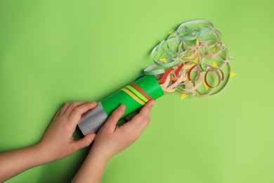 Woman holding party popper with serpentine and confetti on green background, top view