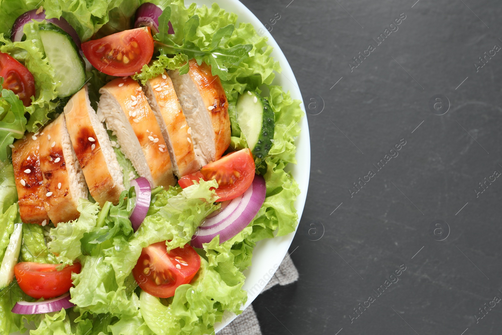 Photo of Delicious salad with chicken and vegetables on black table, top view. Space for text