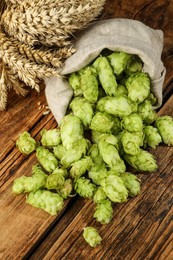 Photo of Overturned sack of hop flowers and wheat ears on wooden table, closeup