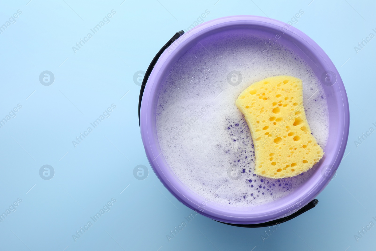 Photo of Bucket with foam and sponge on light blue background, top view. Space for text