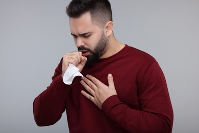Photo of Sick man with tissue coughing on gray background