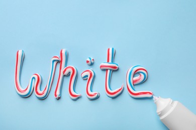 Photo of Tube and word White made of toothpaste on light blue background, flat lay