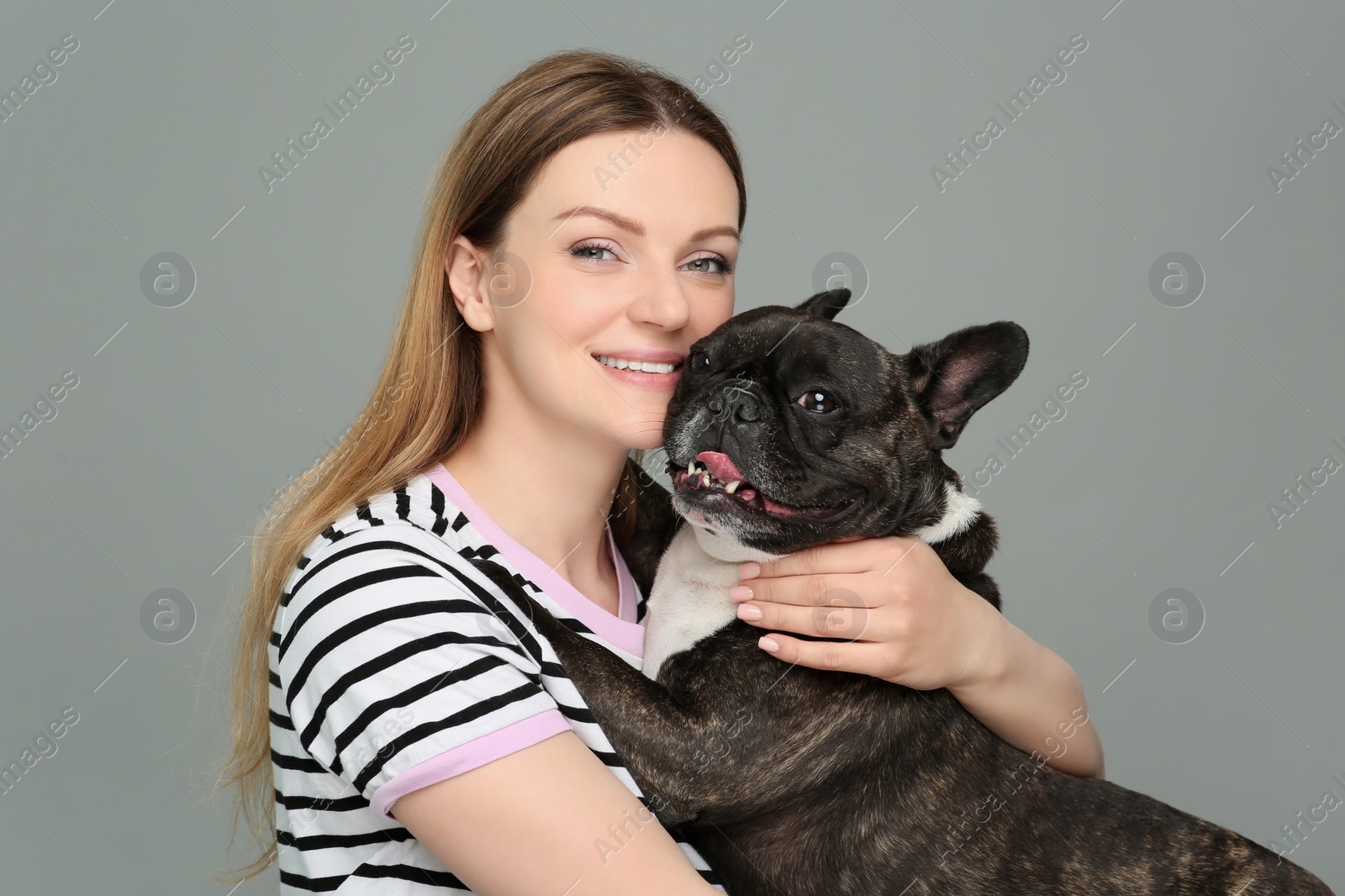 Photo of Portrait of happy woman hugging cute French Bulldog on grey background