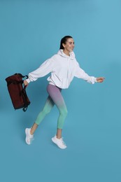 Photo of Beautiful woman with sports bag running on light blue background