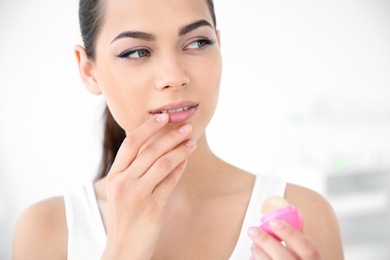 Young woman applying balm on her lips against light background