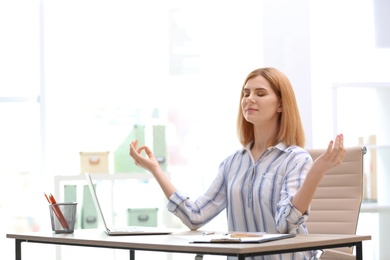 Photo of Beautiful woman meditating at table in office during break, space for text. Zen yoga