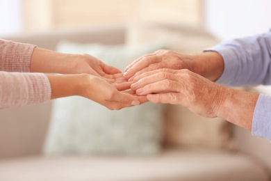 Photo of Young woman holding elderly man hands indoors, closeup. Help service