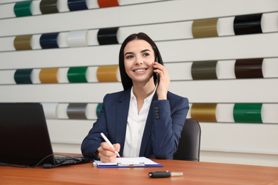 Photo of Saleswoman talking on phone at desk in car dealership