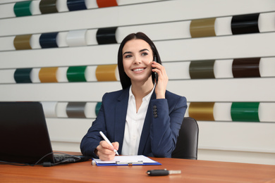 Saleswoman talking on phone at desk in car dealership