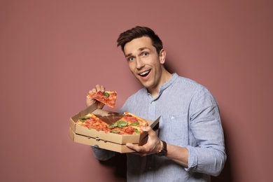 Photo of Attractive young man with delicious pizza on color background