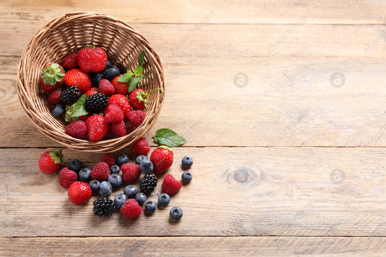 Photo of Wicker basket with many different fresh ripe berries on wooden table, above view. Space for text