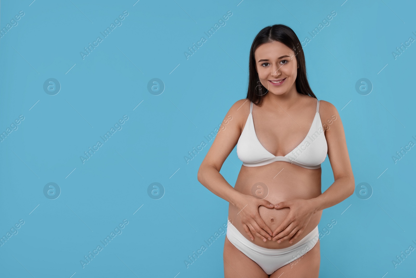 Photo of Beautiful pregnant woman in stylish comfortable underwear on light blue background, space for text