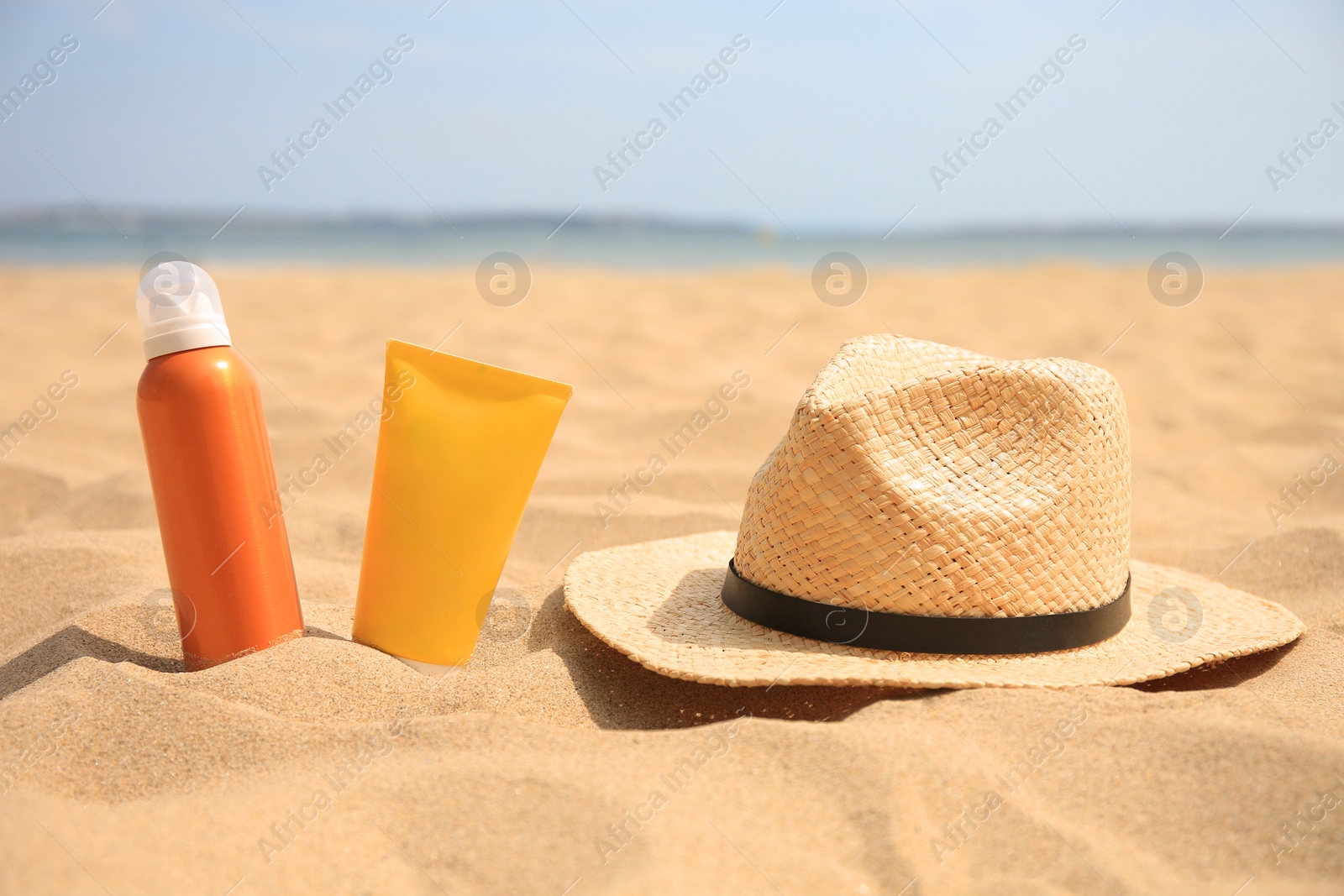 Photo of Sunscreens and straw hat on sandy beach, space for text. Sun protection