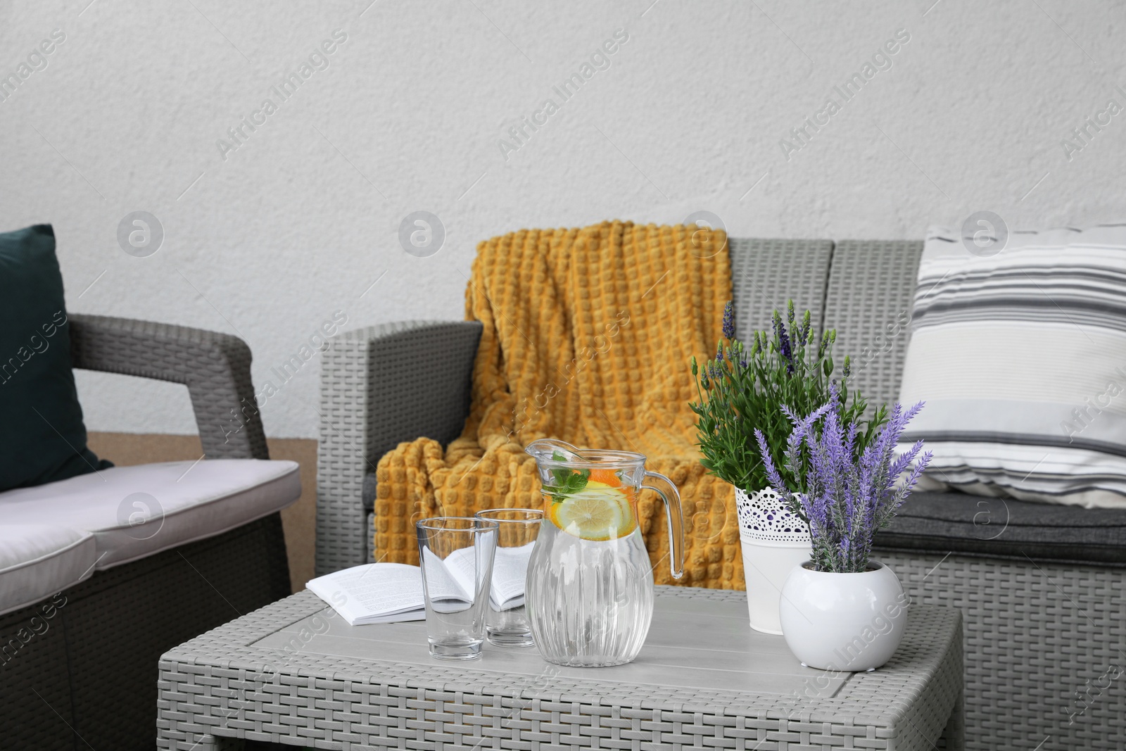 Photo of Table with book, jug of water, potted plants and sofas on outdoor terrace