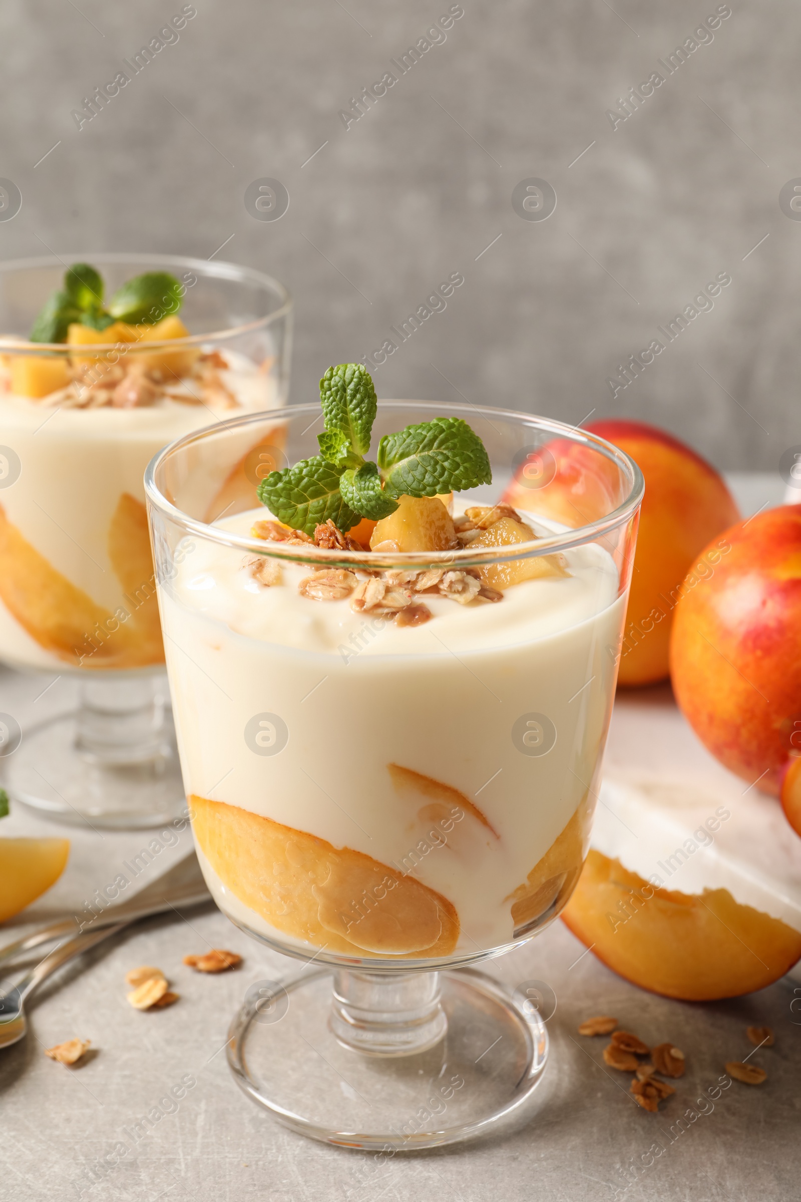 Photo of Tasty peach yogurt with granola, mint and pieces of fruits on light grey table