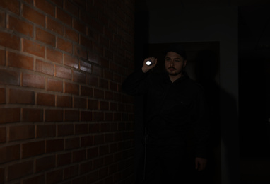 Photo of Male security guard with flashlight in dark corridor