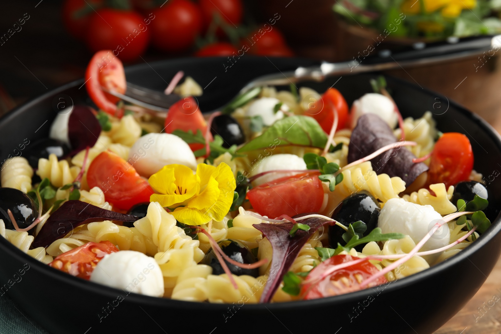 Photo of Bowl of delicious pasta with tomatoes, olives and mozzarella on wooden table, closeup