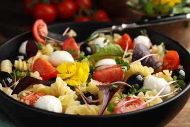 Bowl of delicious pasta with tomatoes, olives and mozzarella on wooden table, closeup