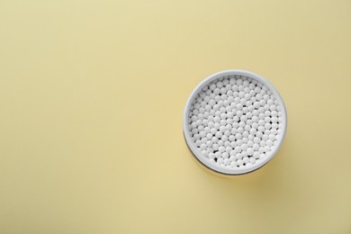 Container with new cotton buds on beige background, top view. Space for text