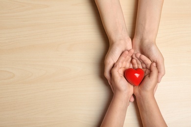 Photo of Woman and child holding heart on beige wooden background, top view with space for text. Donation concept