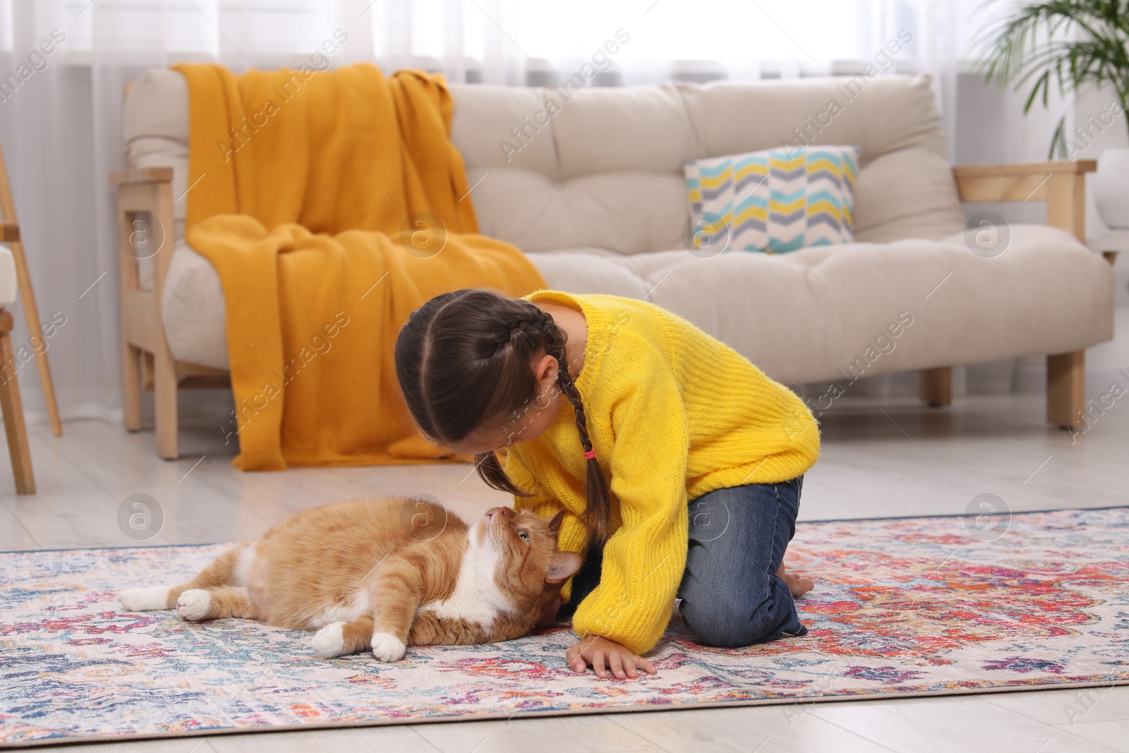 Photo of Little girl and cute ginger cat on carpet at home