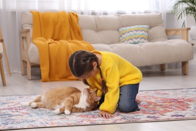 Little girl and cute ginger cat on carpet at home