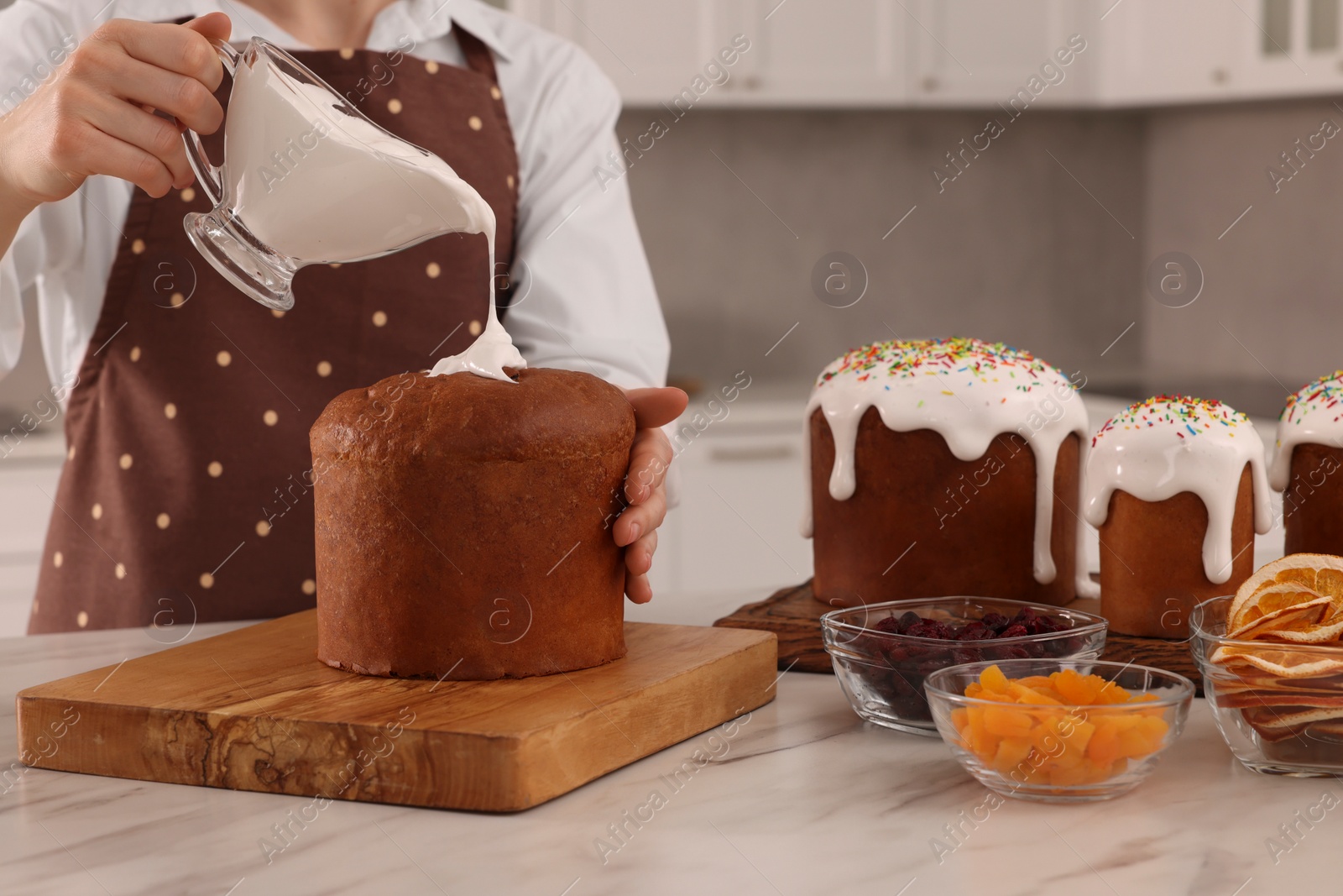 Photo of Woman decorating traditional Easter cake with glaze at white marble table in kitchen, closeup