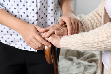Photo of Caregiver and elderly woman with walking cane at home, closeup