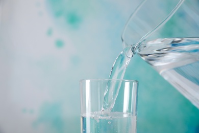 Photo of Pouring water from jug into glass on color background, closeup. Space for text