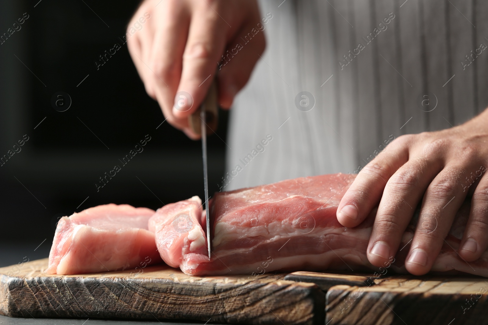 Photo of Man cutting fresh raw meat on wooden board, closeup