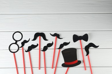 Photo of Fake paper mustaches, bow tie, hat and monocle party props on white wooden background, flat lay. Space for text