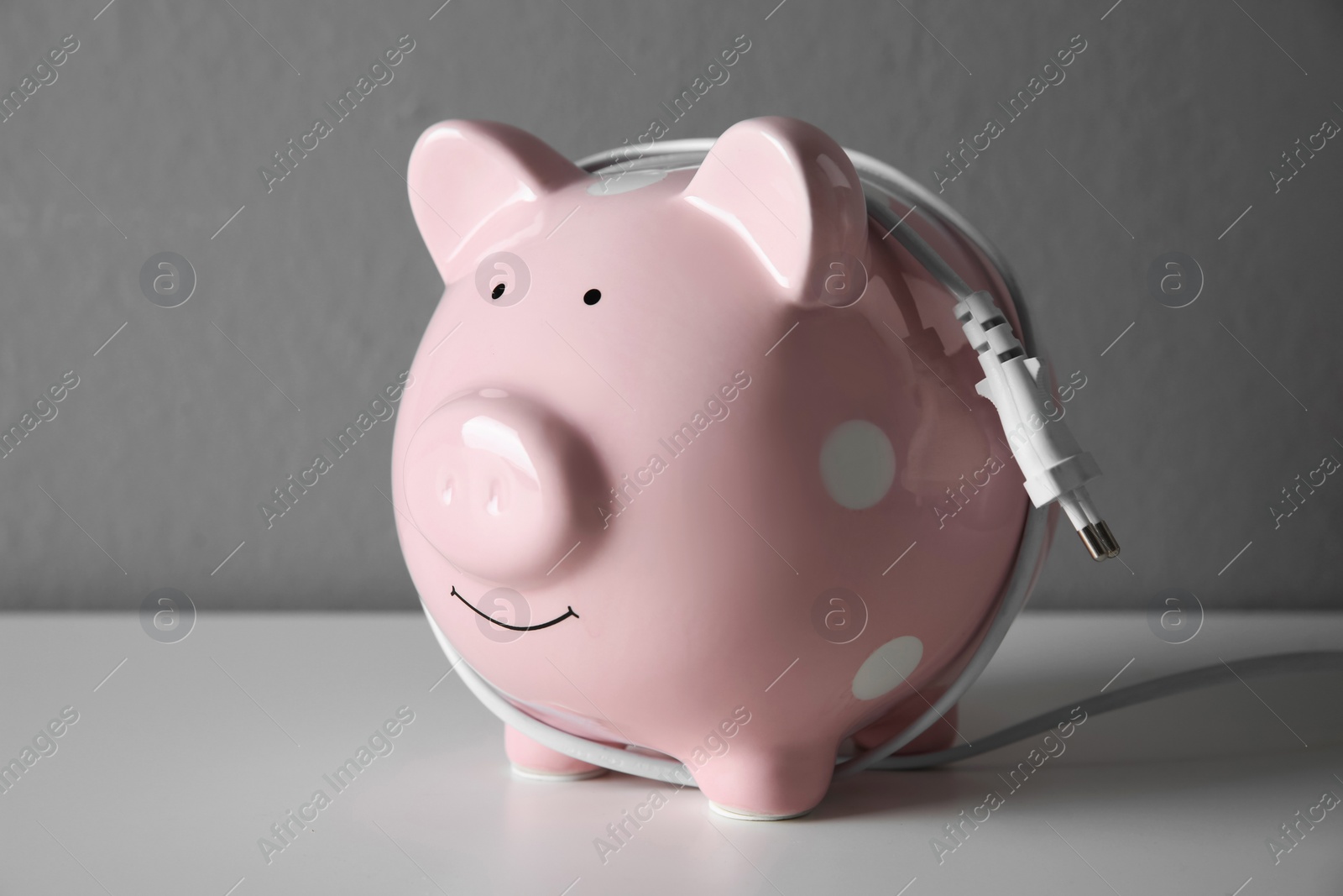 Photo of Piggy bank with power plug on grey table. Energy saving concept