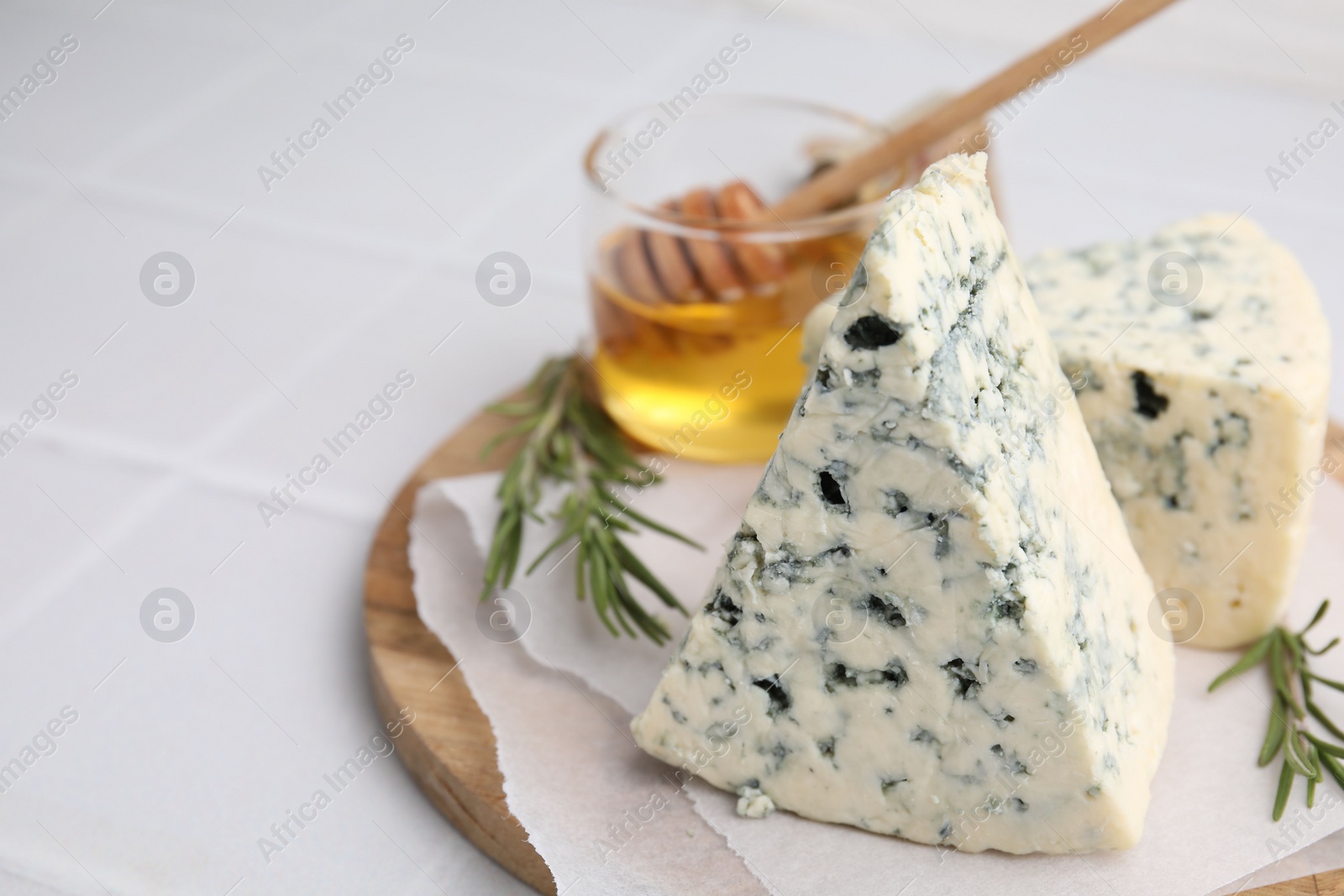 Photo of Tasty blue cheese with rosemary and honey on white tiled table, closeup