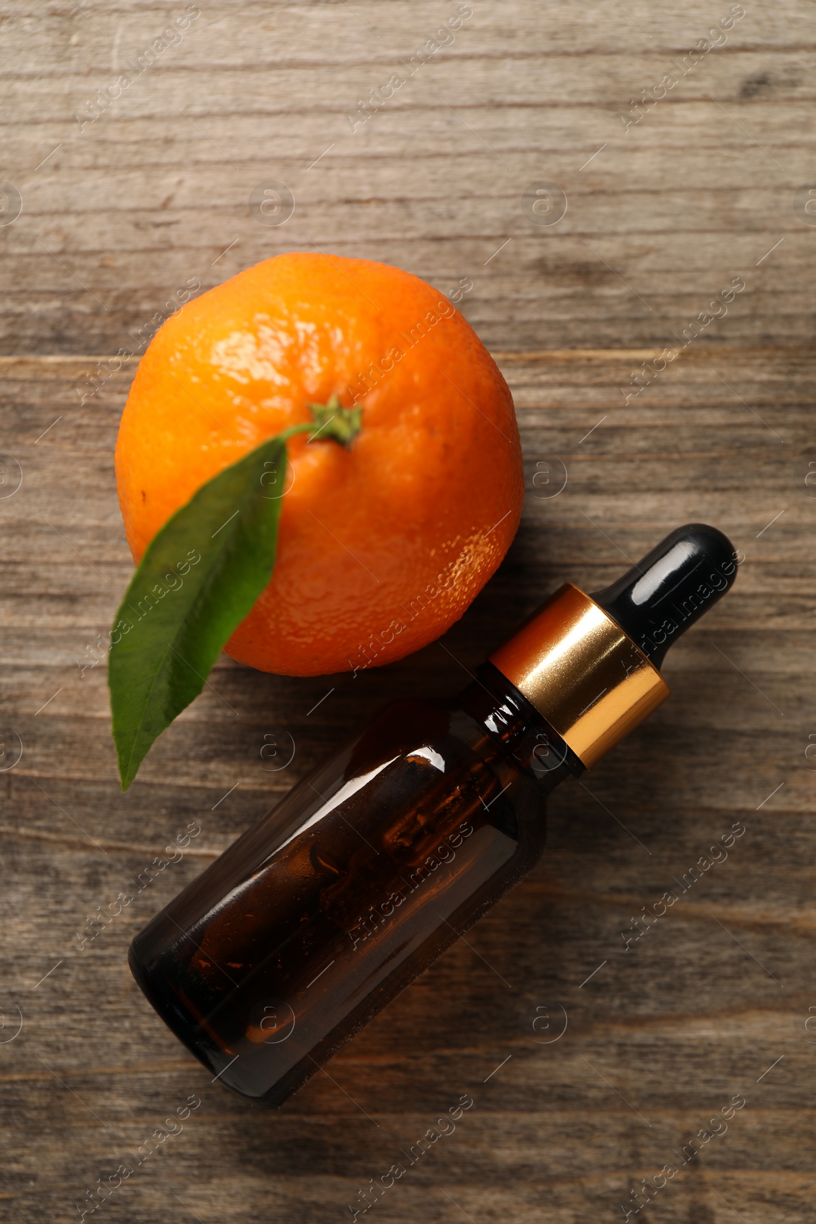 Photo of Bottle of tangerine essential oil and fresh fruit on wooden table, flat lay