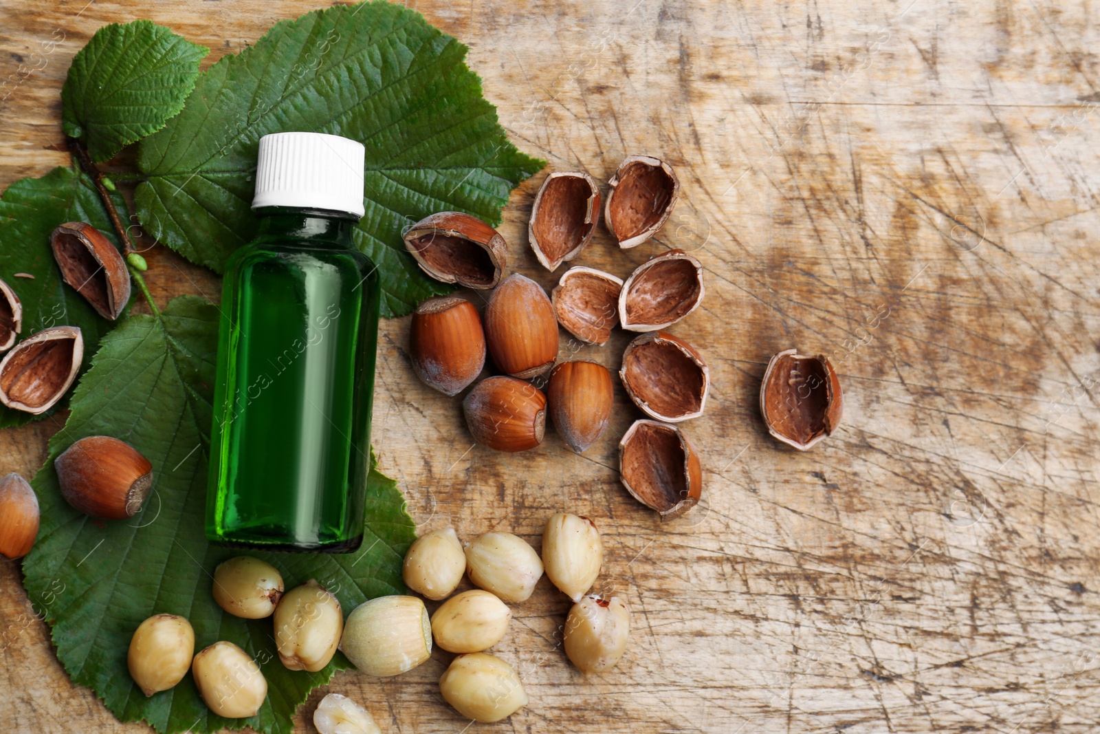 Photo of Bottle of hazelnut essential oil and nuts on wooden table, flat lay