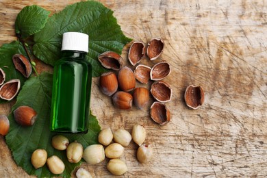 Photo of Bottle of hazelnut essential oil and nuts on wooden table, flat lay