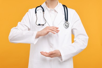 Doctor with stethoscope holding something on orange background, closeup