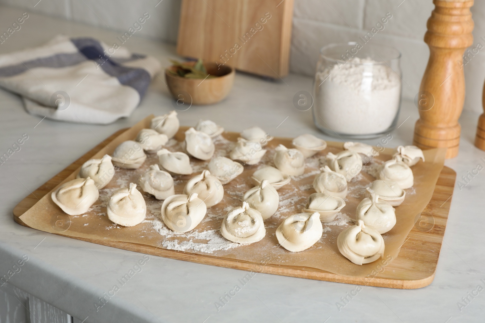 Photo of Fresh uncooked dumplings and flour on white table