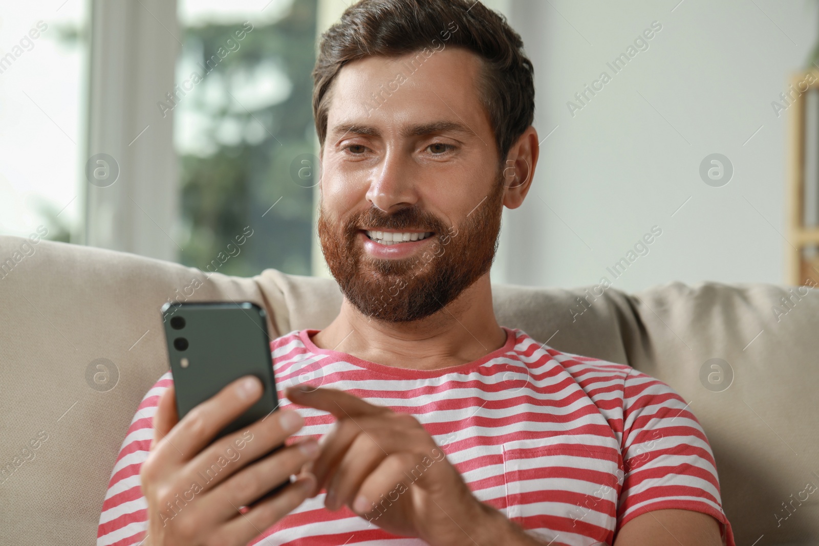 Photo of Handsome man using smartphone on sofa at home