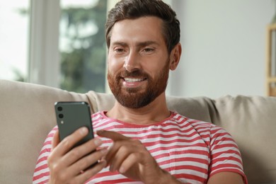 Handsome man using smartphone on sofa at home