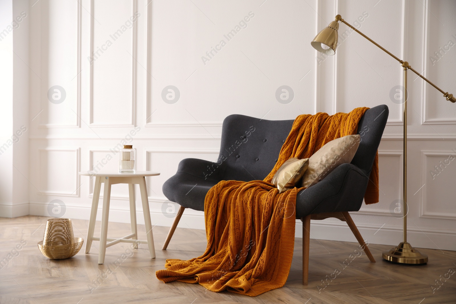 Photo of Comfortable sofa with knitted blanket, coffee table and lamp in stylish room interior