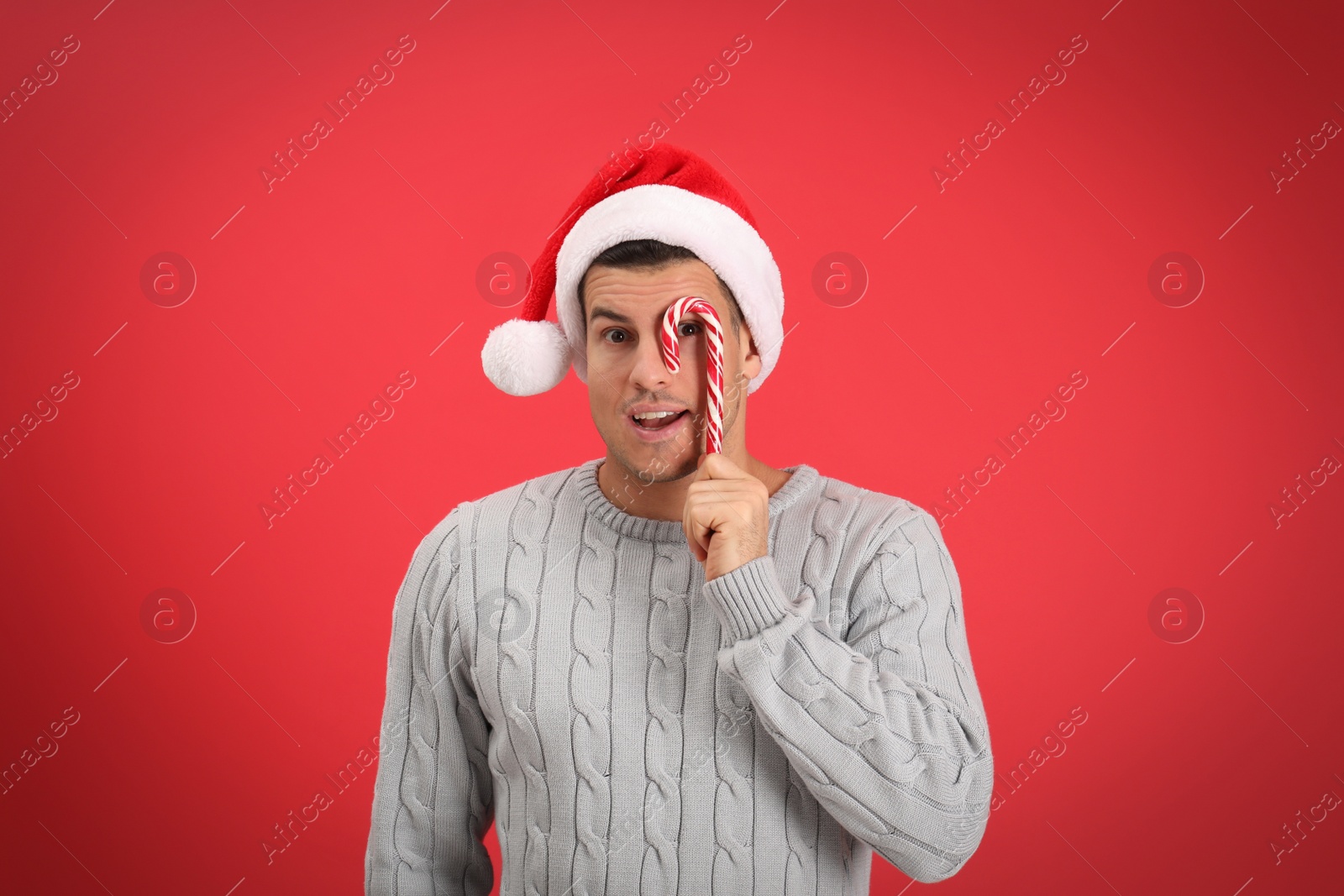 Photo of Handsome man in Santa hat holding candy cane on red background