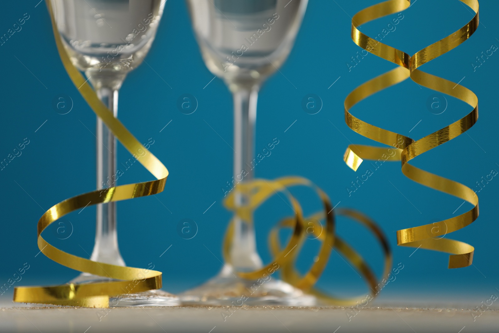 Photo of Glasses of champagne and serpentine streamers on table against blue background, closeup