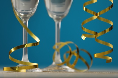 Photo of Glasses of champagne and serpentine streamers on table against blue background, closeup